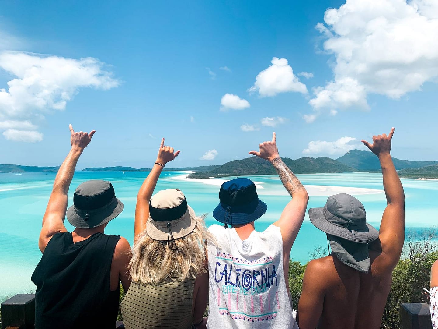 A group on a Whitsundays lookout, arms raised over turquoise water
